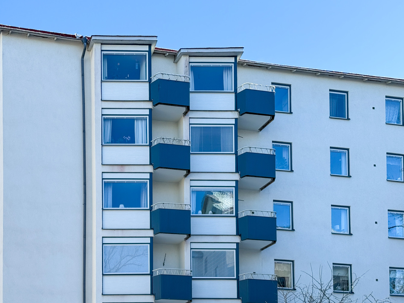 Närbild på fasaden som är vit med blå plåtinklädda balkonger.