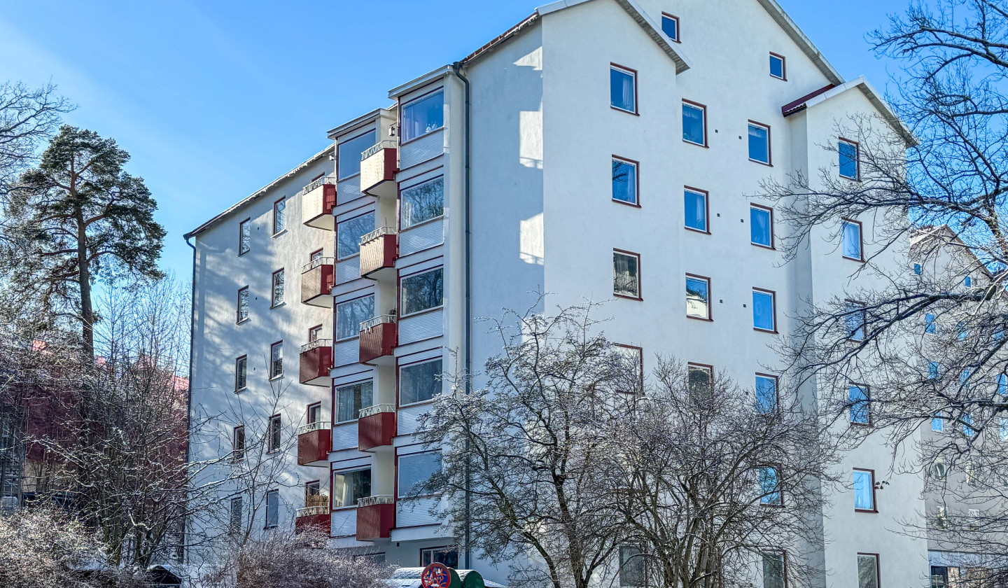 Bild på fastigheten i ljus putsad fasad och röda detaljer runt fönster och på balkonger.