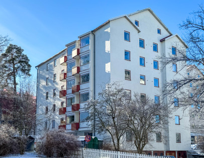 Bild på fastigheten i ljus putsad fasad och röda detaljer runt fönster och på balkonger.