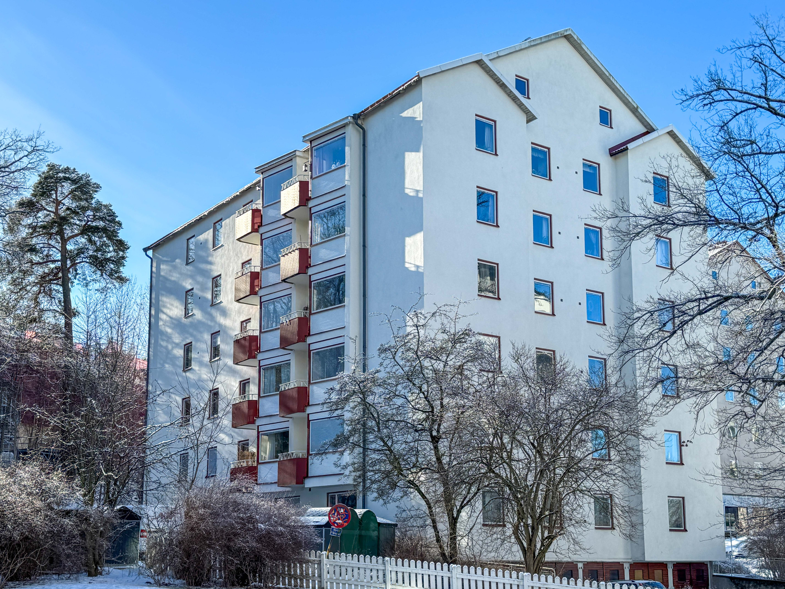 Bild på fastigheten i ljus putsad fasad och röda detaljer runt fönster och på balkonger.